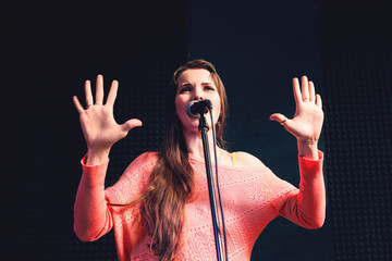 Young protesting woman on stage with microphone. Pretty woman screaming into mic, hands rised in stop gesture. Violently protesting young beautiful woman on stage