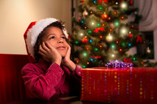 Afroamerican Boy Near Christmas Present. Black Kid Beside Christmas Present. Wait Until It's Time. Holiday For Everyone.