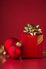 Wall Mural - red gift box with golden ribbons and xmas baubles on red background. merry christmas. space for text