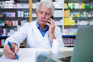 Wall Mural - Pharmacist talking on mobile phone while writing prescriptions