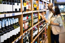 Couple Looking At Wine Bottle In Grocery Section