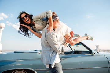 Wall Mural - Happy young man carrying his woman near vintage car