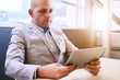 © nakophotography - Business man holding and using a high tech tablet while seated at a conference table early in the morning with a window behind him and light coming in through the glass.