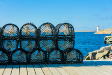 Stack Of Lobster Cages Or Pots On Pier With The Swedish Town Of Mollesund Lighthouse In Background.