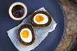 © Mint Images - Village pub food. A blue dish with a fresh made scotch egg cut in to two and a pot of sauce.