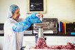 © Mint Images - Woman working in a butchery, wearing protective clothes and gloves, putting minced meat into a meat grinder.