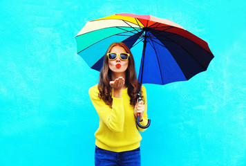 Pretty young woman with colorful umbrella sends air sweet kiss i