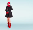 Winter fashion woman with red hat,scarf,handbag purse,boots, wearing black coat and gloves isolated on light blue background. copy space. 