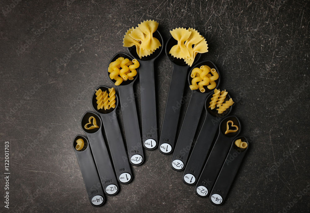 Different dry pasta on measuring spoons