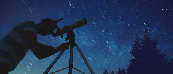 Wall Mural - man looking at the stars with telescope beside him.