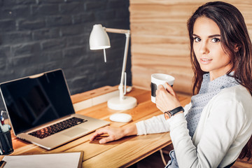 Portrait of relaxed young woman sitting at her desk holding cup of coffee