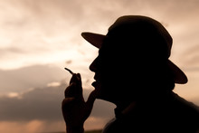 Silhouette Of A Man Smoking A Cigarette On The Sunset Background