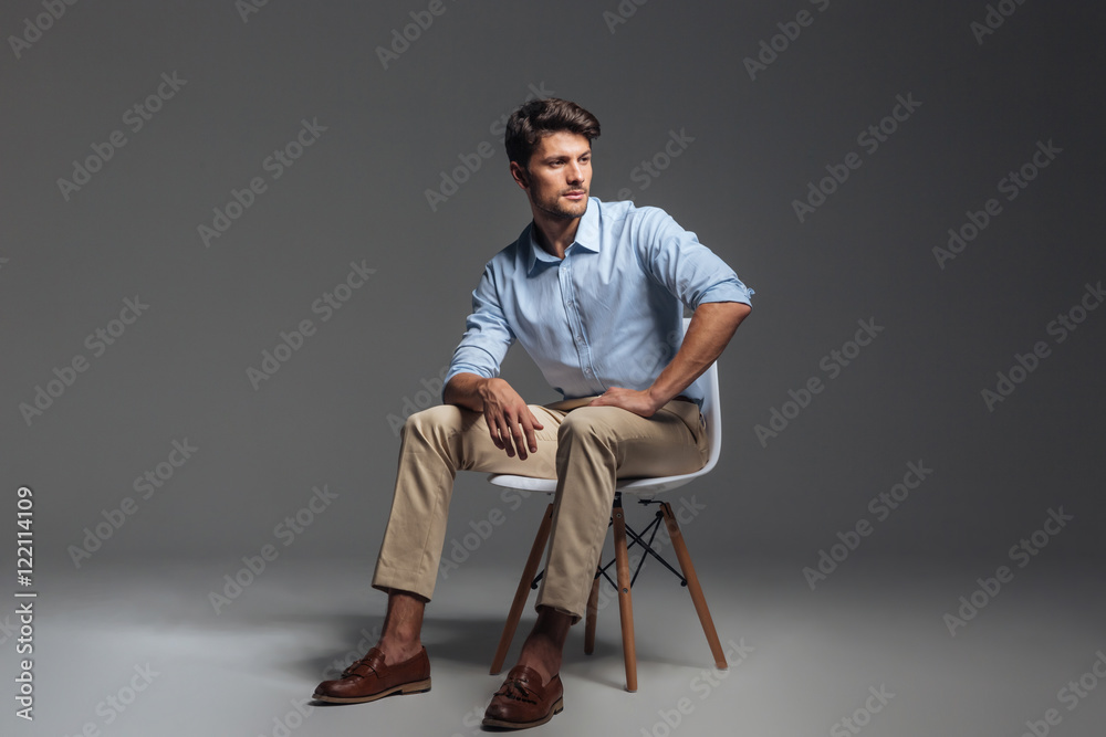 Pensive brunette man in blue shirt sitting on the chair - obrazy, fototapety, plakaty 