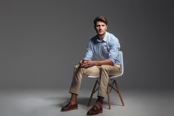 Pensive brunette man in blue shirt sitting on the chair