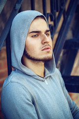 Wall Mural - Conceptual art portrait of beautiful handsome young middle east brunette man with blue eyes, beard, wearing blue hoodie, outside in street looking away