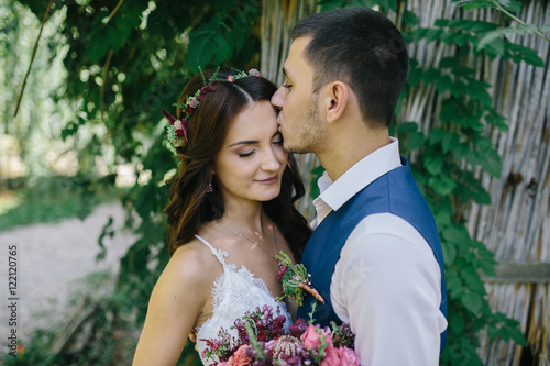 Fotografie, Obraz happy groom in a dark blue suit kisses a beautiful bride in a white wedding dres