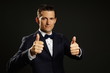 © petrdlouhy - Young businessman in suit shows you thumbs up on gray background