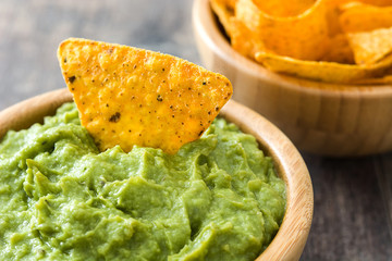 Wall Mural - Guacamole in a bowl and nachos on wooden background

