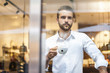 © Westend61 - Businessman holding cup of coffee looking through window