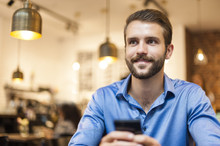 Smiling Young Man With Cell Phone In A Cafe