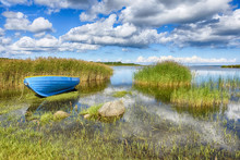 Blue Boat On The Shore Of The Lake In The Tall Grass