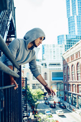Wall Mural - Conceptual art portrait of beautiful handsome pensive sad tired gothic young middle east brunette man with beard in hoodie, standing on staircase in city urban looking down on street