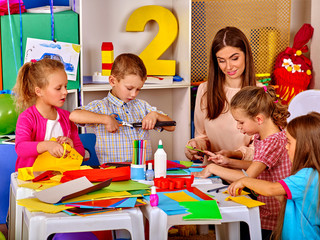 Wall Mural - Group children with teacher are making something out of colored paper on table in primary school. Children craft lesson in primary school.