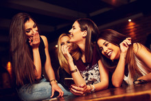 Group Of Young Women Friends Having Fun Looking At Something Funny On Their Smart Phone And Laughing