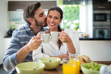 Man kissing on woman cheeks while having breakfast