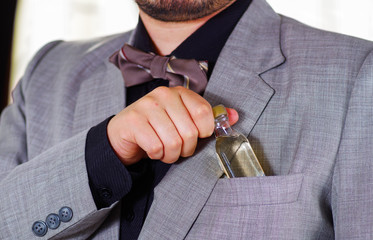 Closeup man's chest area wearing formal suit and tie, placing small liquor bottle in jacket pocket, men getting dressed concept