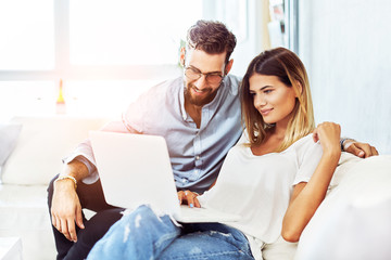 Young smiling couple sitting on the sofa and surf the Internet