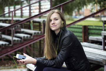 Canvas Print - Young beautiful girl look and listening music on your mobile phone  the old stadiums bench