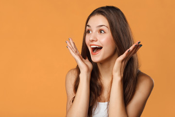 surprised happy beautiful woman looking sideways in excitement. isolated on orange background