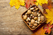 Various Kinds Of Nuts - Dried Fruit - Over Wooden Background With Autumn Leaves