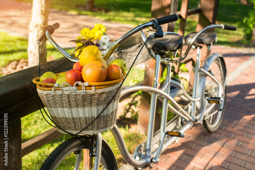 Plakat Kosz owoców na rowerze. Rower i bukiet na ogrodzeniu. Zorganizuj piknik dla dwojga. Ciepłe dni w sierpniu.
