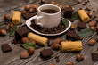 two small white cups of coffee with, cookies, cocoa beans, slices of chocolate, hazelnuts and green leaves on wooden background