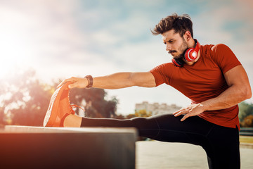 Young man streching legs on outdoor stall bar