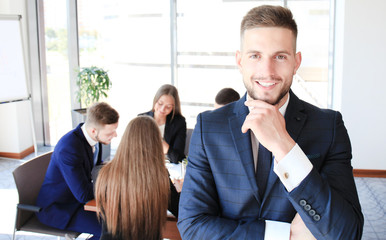 Young businessman standing in office with his collegue on the background