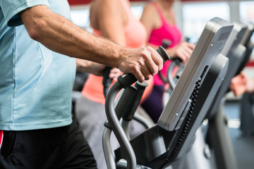 Senioren trainieren am Crosstrainer im Fitnessstudio mit Fitnesstrainer