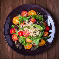 Wall Mural - Fresh healthy salad with quinoa, cherry tomatoes and mixed greens (arugula, mesclun, mache) on wood background top view. Food and health. Superfood.