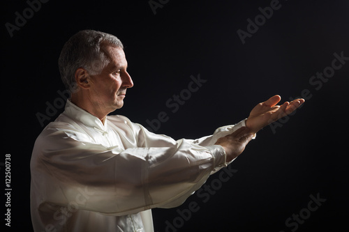 Zdjęcie XXL Starszy mężczyzna cieszy się wykonywania Tai Chi w pomieszczeniach.