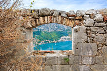 View Of The Coastal Town At Foot Of Mountains And Sea Bay From The Window In Old Stone Wall Of A Medieval Fortress In Adriatic Coast, Kotor, Montenegro.