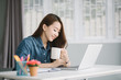 © uinmine - Smiling asia woman use laptop hand holding a cup