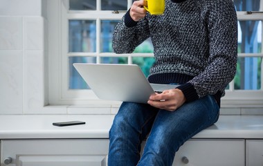 Poster - Man using laptop while having coffee in the kitchen