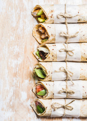 Wall Mural - Tortilla wraps with various fillings on shabby painted board over white wooden background, top view, copy space, vertical composition. Healthy snack or take-away lunch bites