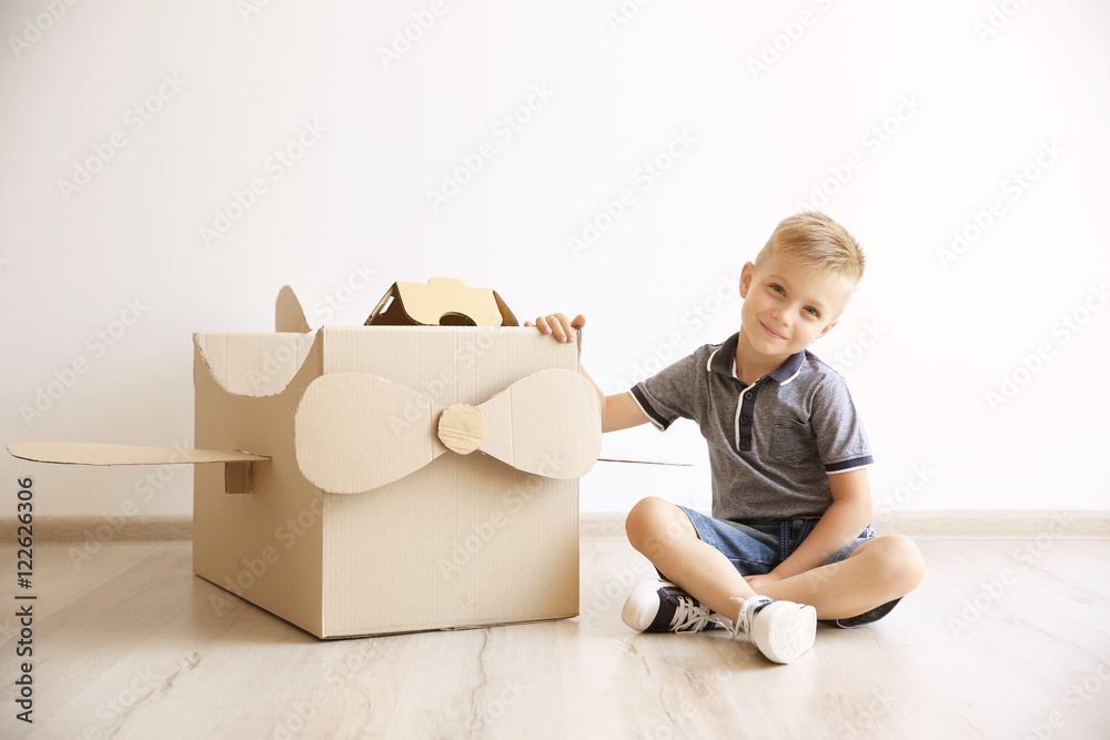 Little boy playing with cardboard airplane on white wall background
