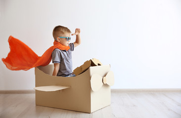 Little boy playing with cardboard airplane on white wall background