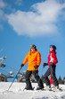© anatoliy_gleb - Couple holding skis smiling on mountain top together at a winter resort with ski lifts and blue sky in background. Man is wearing orange jacket, female in red jacket, both is wearing helmets
