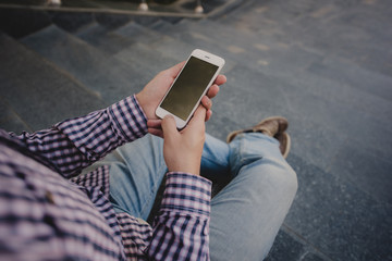 young Man with the phone in his hand sitting on the steps. top view