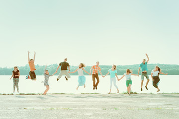 group of people holding hands and jumping at the park near the lake. smiling girls and boys having f